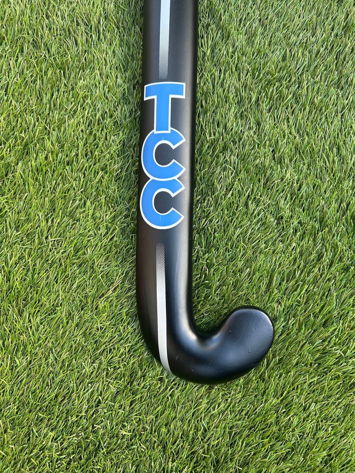 TCC Black and blue hockey stick on a grass field featuring the stick head