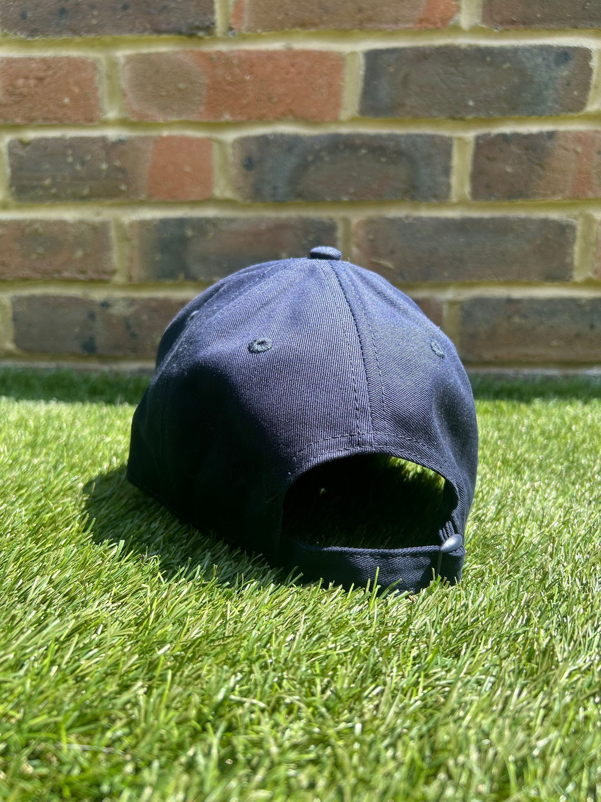 TCC Navy Adjustable Cap rear view positioned on the grass