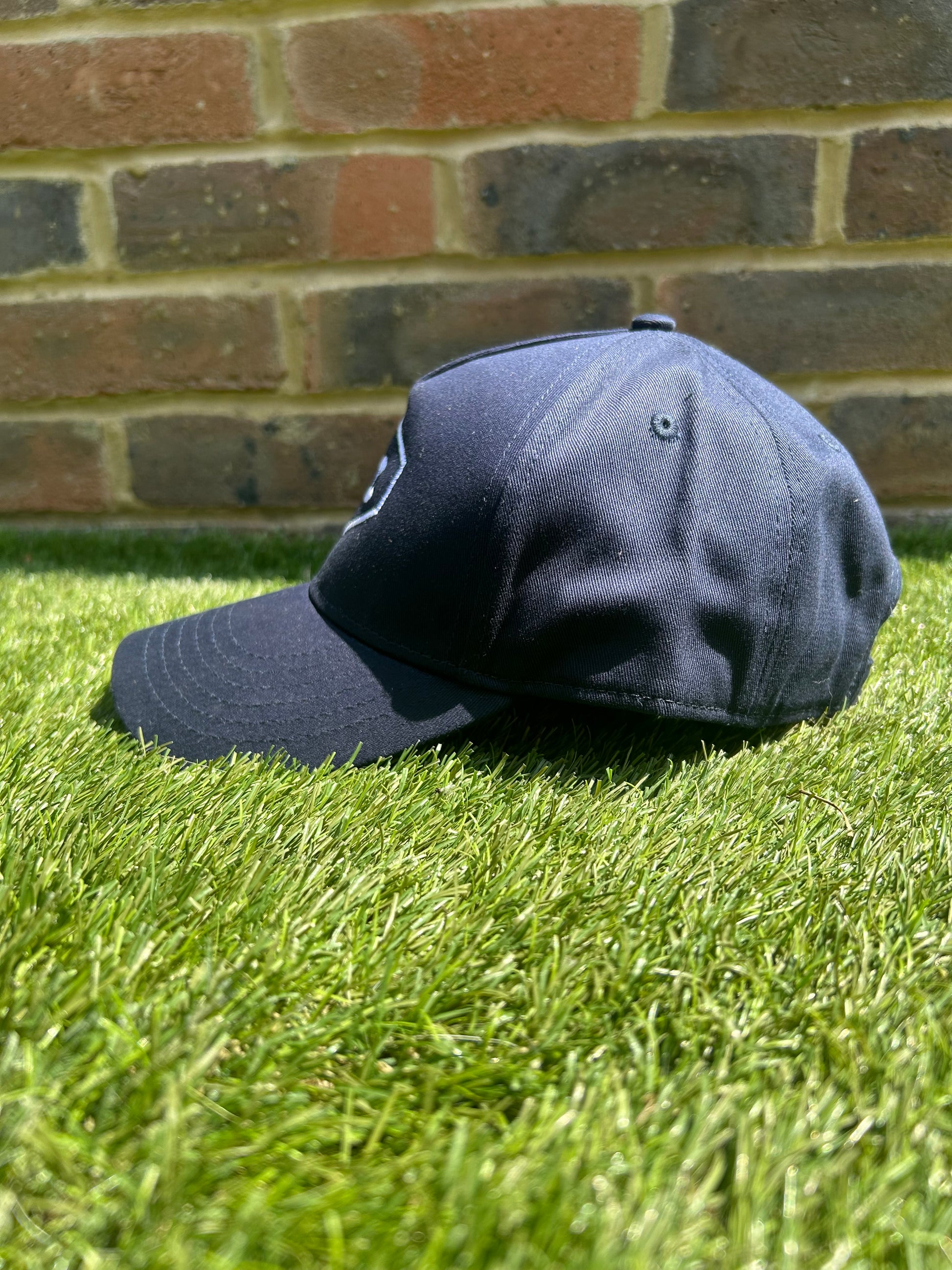 TCC Navy Adjustable Cap side on view positioned on the grass
