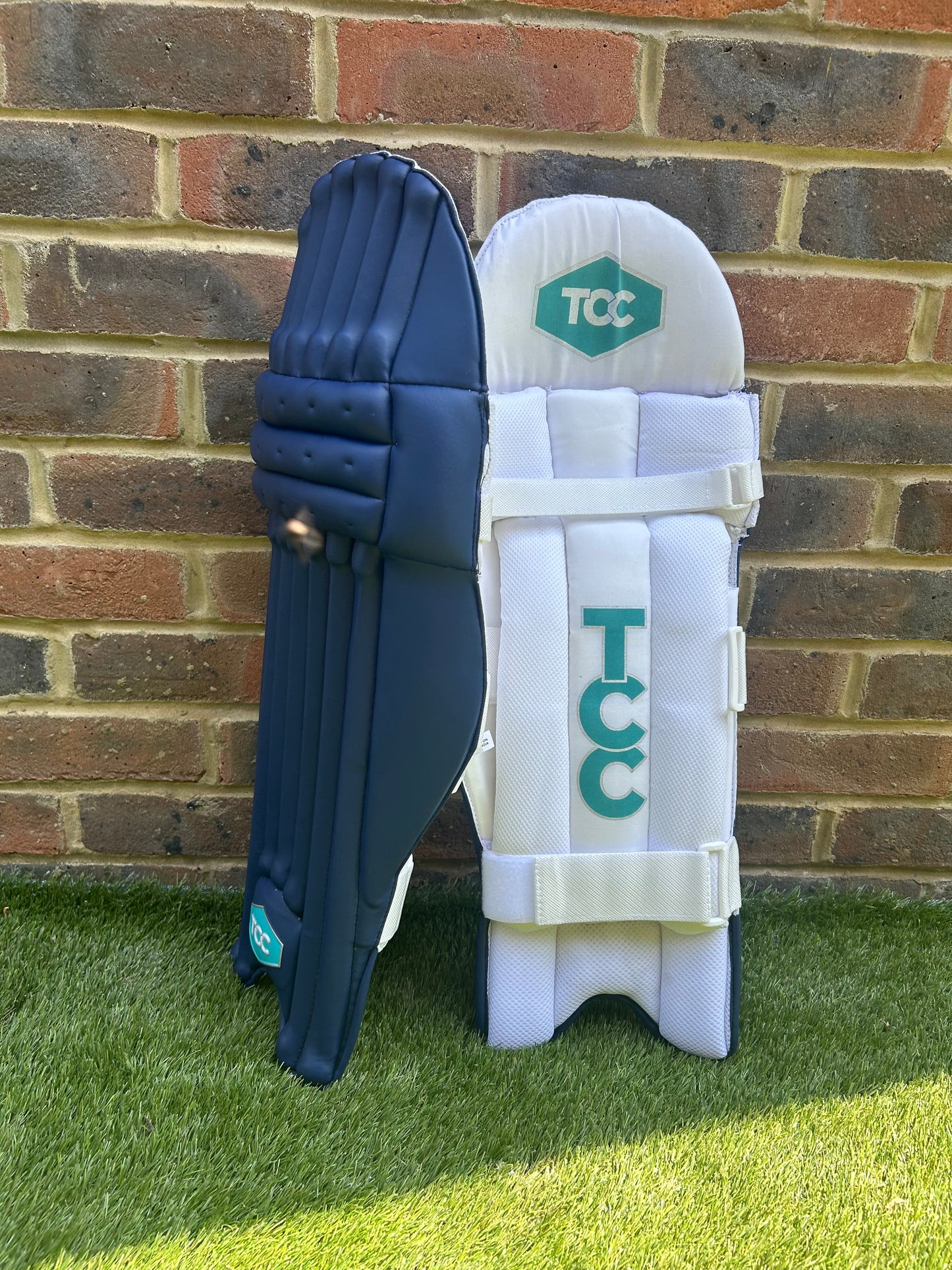 TCC Youth Navy Batting Pads with Teal Logo and side on profile showing one pad leaning against the other