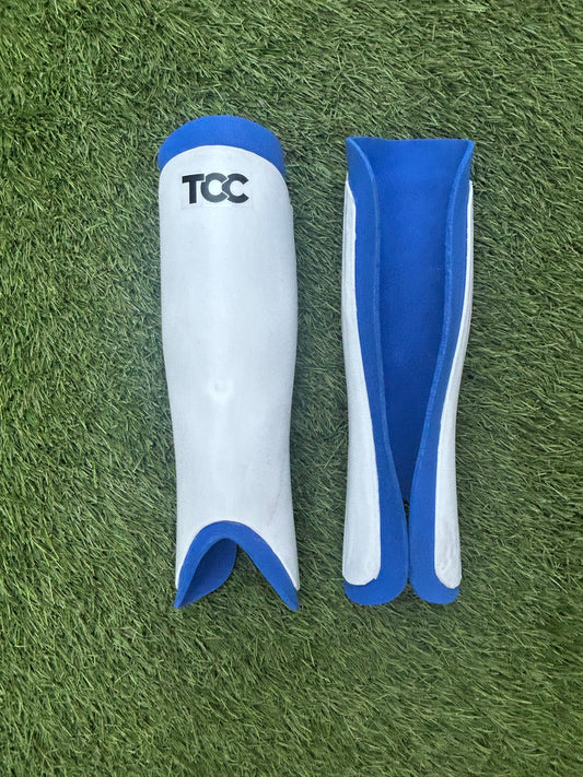White and blue shin guards with 'TCC' branding on a grassy background